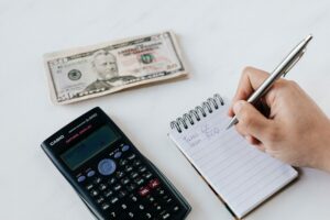 Persona tomando notas en un cuaderno junto al dinero y la calculadora que representa: Independencia Financiera
