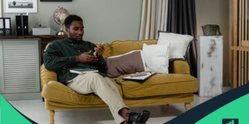 Hombre sentado en el sofá, contando dinero que representa: ¿cómo ganar más dinero?